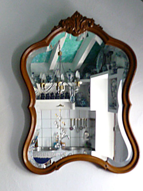 Ein Spiegel in einem geschwungenen Rahmen. Er zeigt eine Küche.