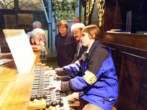 Eine Frau spielt Orgel. Fünf Menschen hören aufmerksam zu.