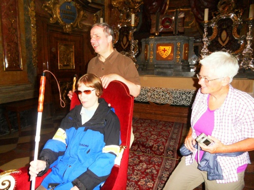 Drei Menschen vor dem Barockaltar des Doms, eine Frau sitz auf einem prächtigen Stuhl.