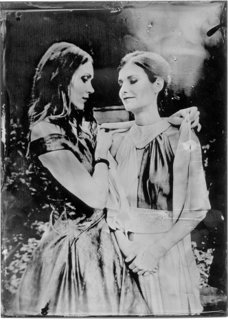 Eine junge Frau mit langen Haaren legt einer jungen Frau mit kurzen Haaren eine Stola um. Schwarz-Weiß