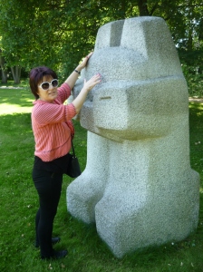 Eine Frau mit Sonnenbrille betastet eine Steinskulptur im Park