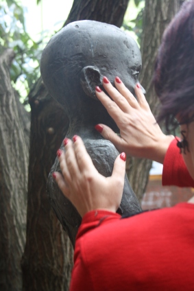 Eine Frau mit rotlackierten Fingernägeln betastet den Kopf einer Bronzeplastik